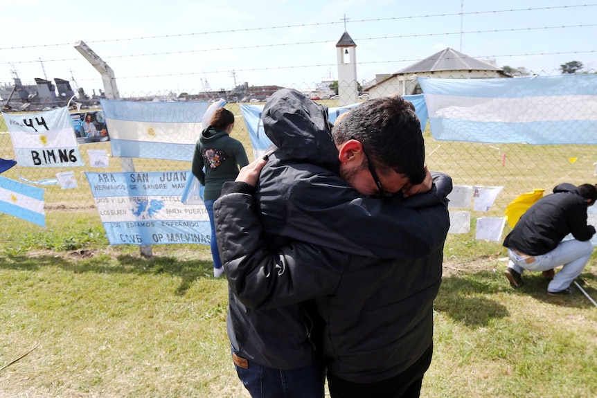 Relatives and friends of Alejandro Damian Tagliapietra hug near banner saying  "Camarades, be strong"