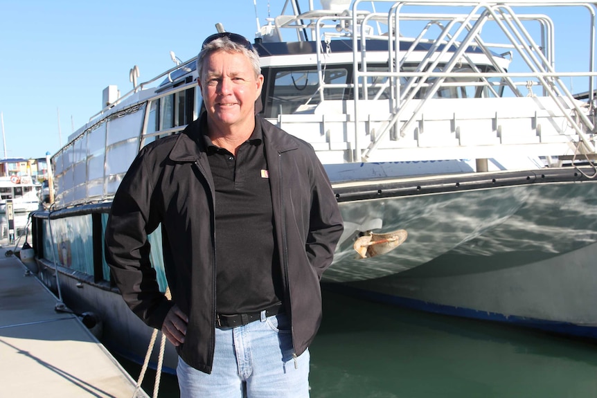 A man in a black coat standing in front of a boat.