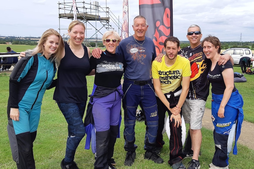 A group of skydivers poses for a photo on the ground.