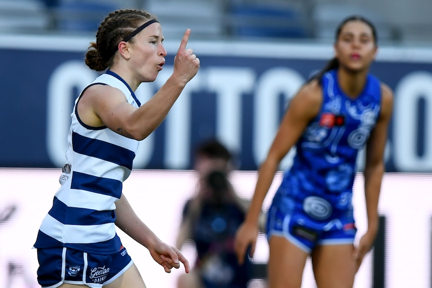 A Geelong AFLW player runs back to the middle pointing her finger to the sky in celebration after a goal.