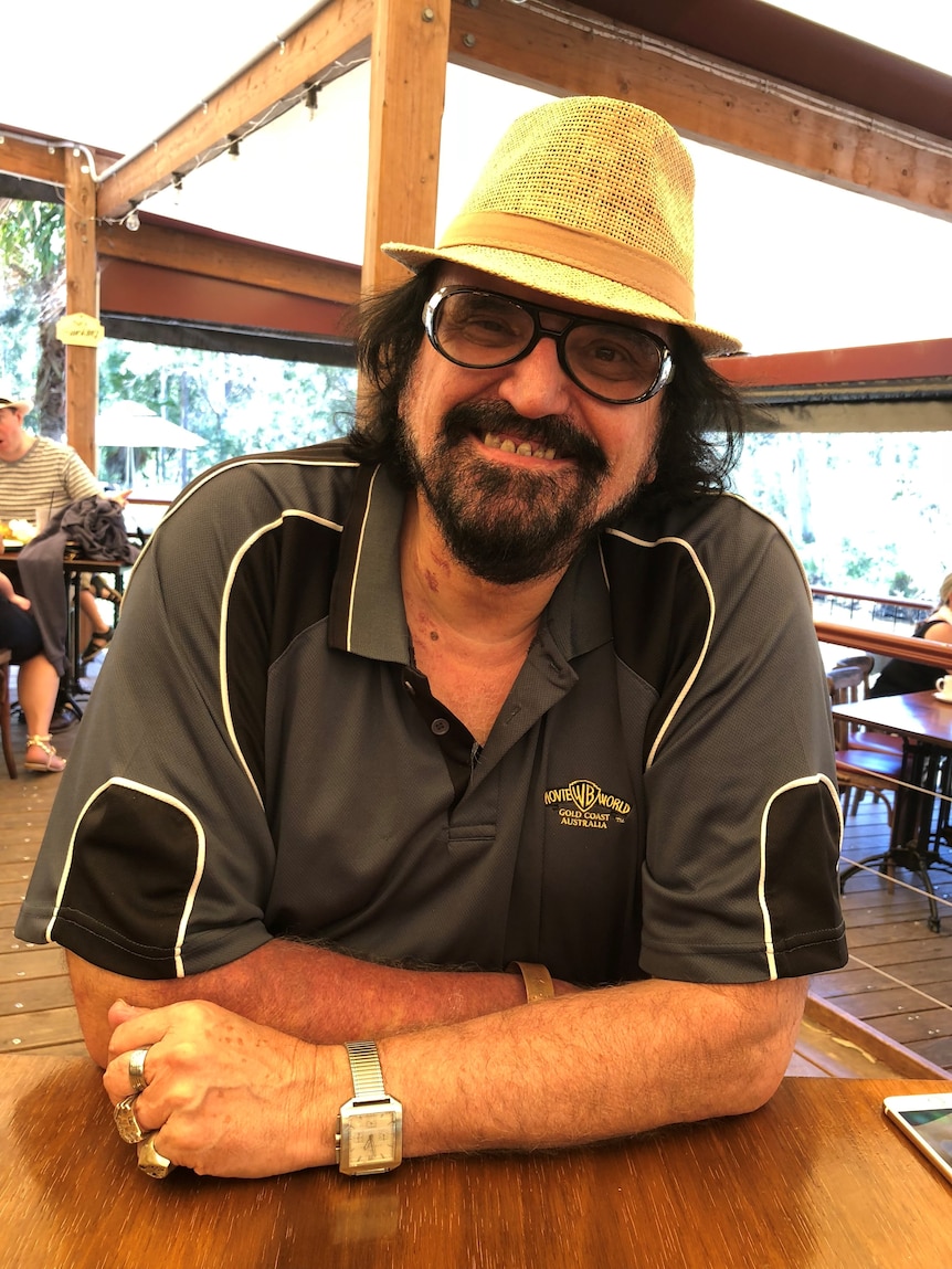 A man wearing a black and gray shirt and hat, leaning forward with a big smile.