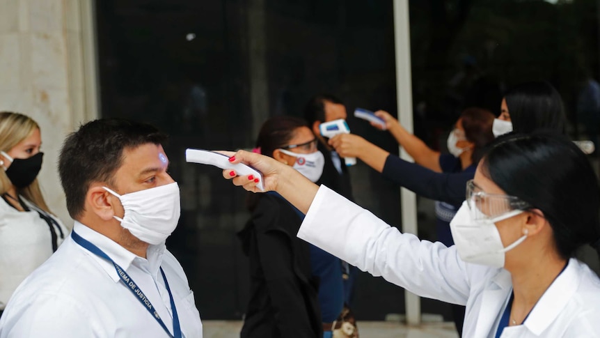 People standing in a row wearing masks get their temperatures checked in Paraguay.