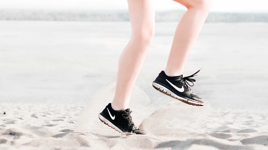 A person wearing sneakers runs on the spot on soft beach sand.