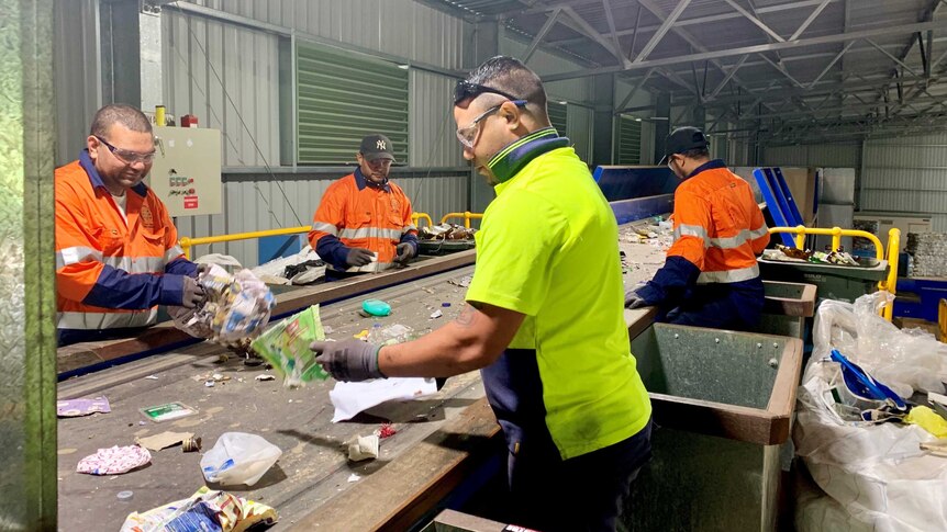 Workers at the Cherbourg Material Recovery Facility sort through recyclable materials on a conveyer belt.