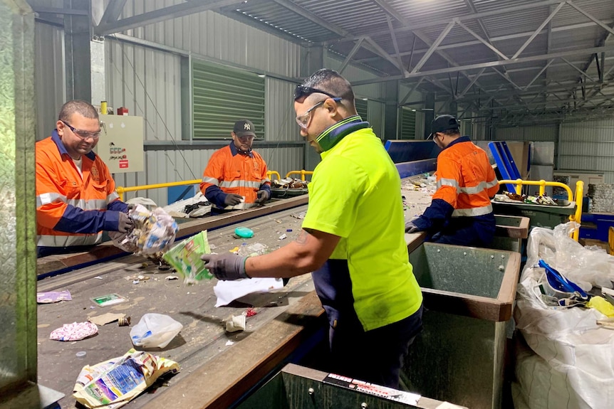 Workers at the Cherbourg Material Recovery Facility sort through recyclable materials on a conveyer belt.