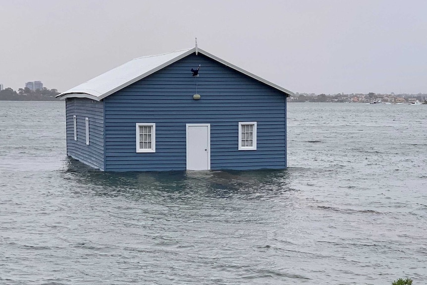 A blue boathouse in the middle of a river with its jetty underwater.