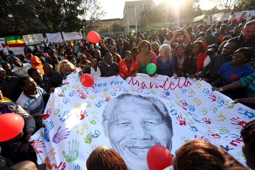 Well-wishers outside hospital in Pretoria hold a giant banner showing Nelson Mandela.