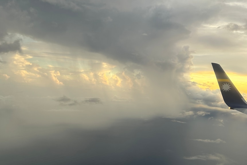 Huge amounts of rain fall from clouds into an ocean. The tip of an airplane's wing is visible on the right