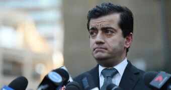 Sam Dastyari frowns while standing in front of a group of microphones