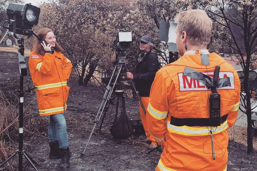 Crew in orange protective clothing with camera and lights set up in burnt out bush.