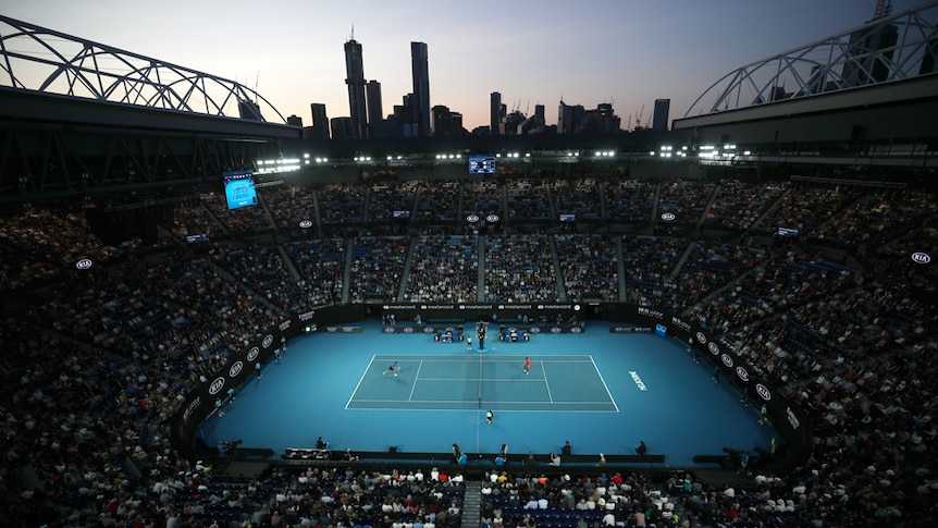 A wide angle view looking down at the stands and showcourt at Rod Laver Arena with the Melbourne skyline in the distance.