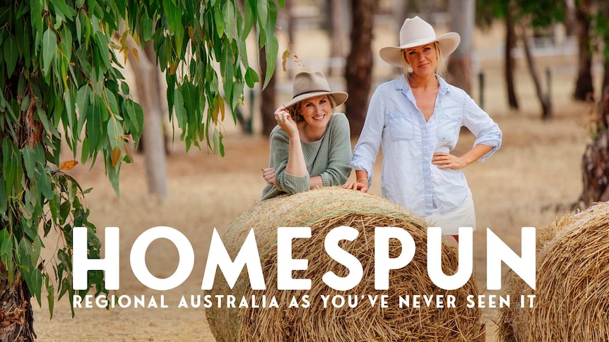 Two women wearing hats standing behind a hay bale in the countryside