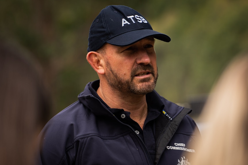 A close-up side profile shot of a man wearing a uniform, including a jacket and a cap.