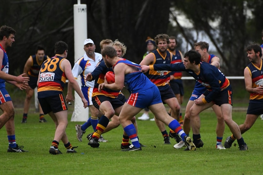 A group of football players try to take another player who is holding a red football.