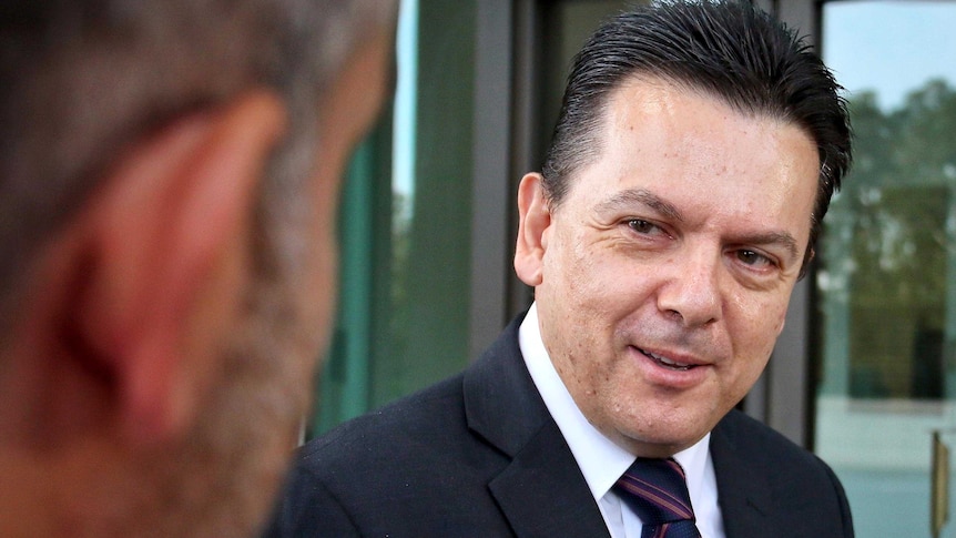 Nick Xenophon smiles as he speaks to a reporter, whose head is also in shot, out of focus in the foreground.