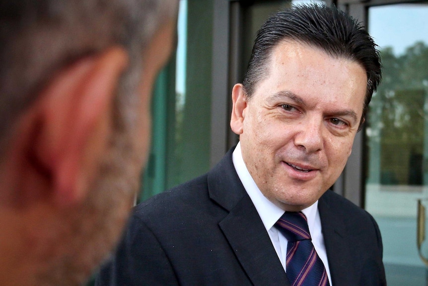 Nick Xenophon smiles as he speaks to a reporter, whose head is also in shot, out of focus in the foreground.