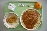 Spaghetti in a bowl on a green prison food tray, with an orange and a carton of milk.
