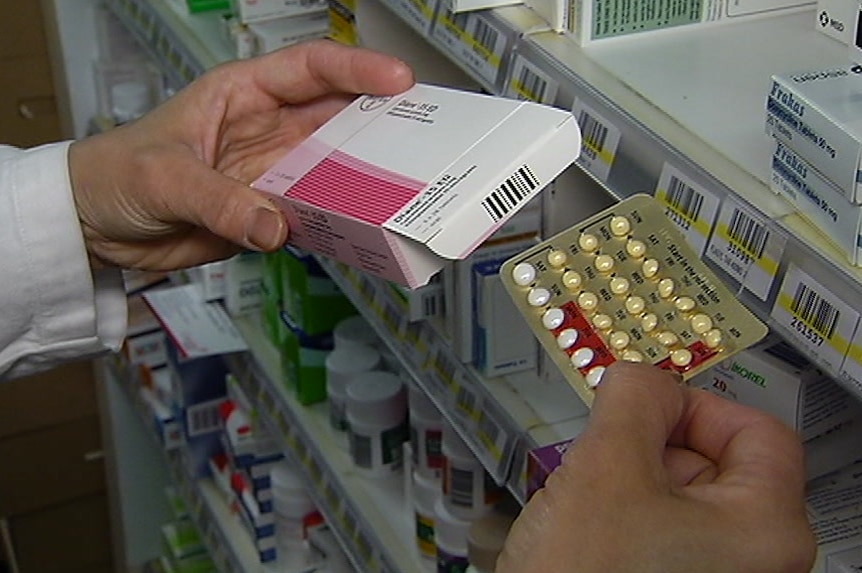 The hands of a person in a white pharmacist's coat takes a row of pills in foil out of a box.