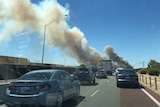A car in a traffic jam on a freeway with a big plume of smoke ahead.