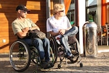 Two men in wheelchairs look to the right of the grame outside a house in Sweden.