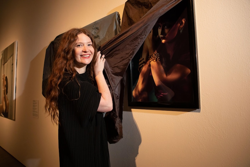 A woman in black takes a cover off a precious painting in a gallery.