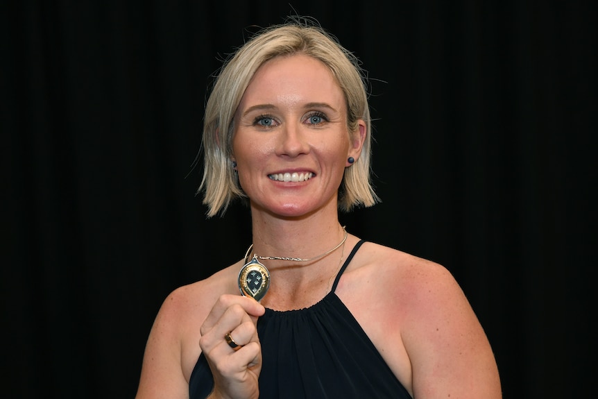 Beth Mooney, in a black dress, smiles and shows off a medal.