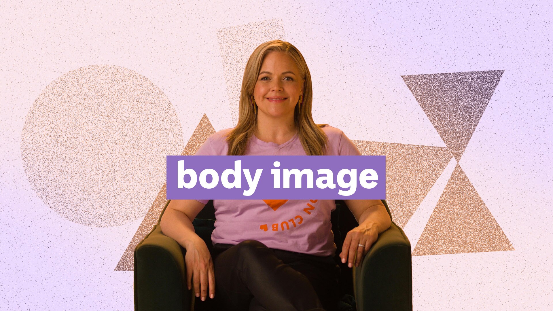 Taryn Brumfitt sits on a chair smiling at the camera.