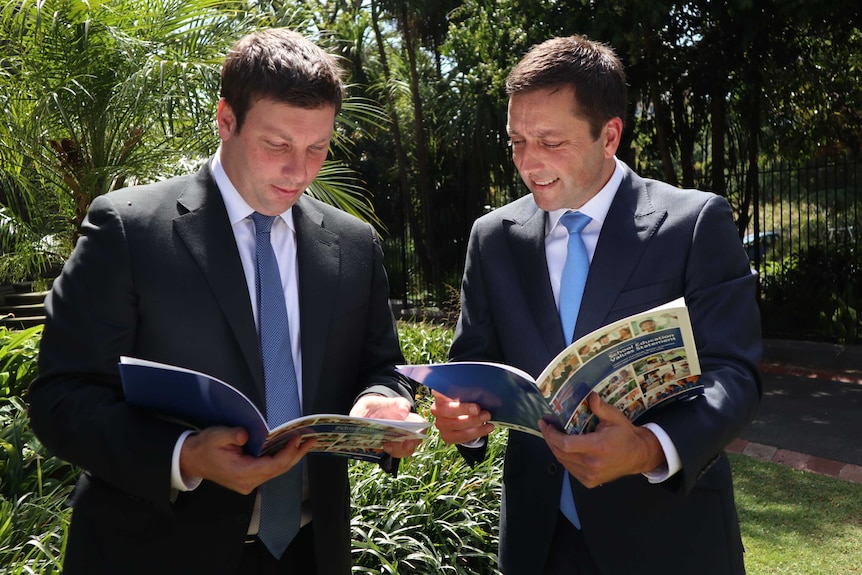 Tim Smith and Matthew Guy, dressed in suits, each read a copy of the School Education Values Statement.