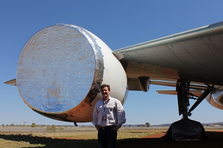 A man stands next to a taped up aircraft engine.