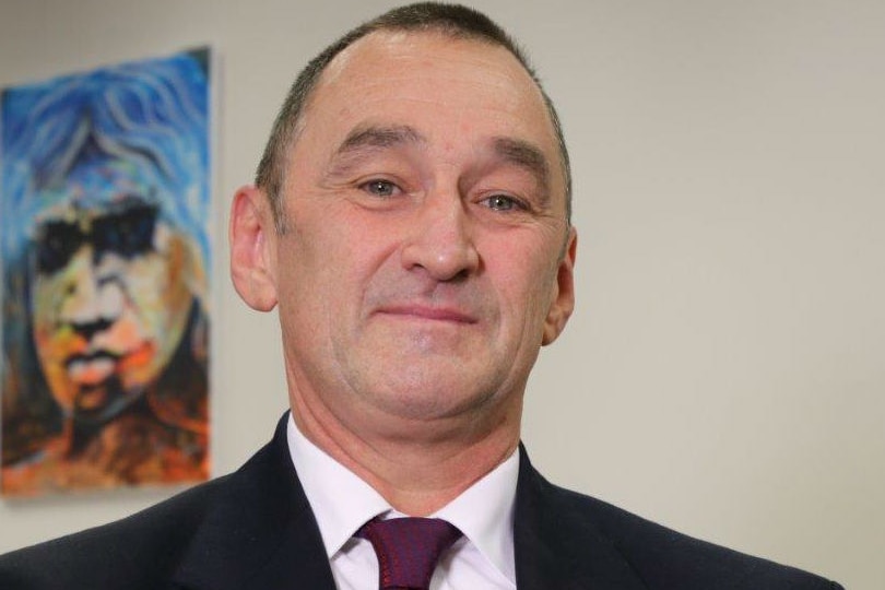 head and shoulders shot of middle aged man smiling at camera with colourful painting on wall in background