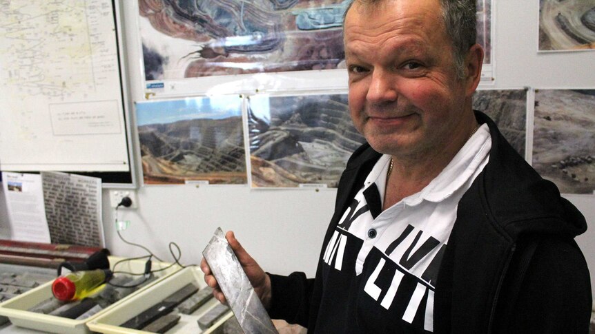 A man holding an ore sample smiles for the camera.