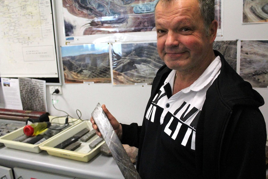 A man holding an ore sample smiles for the camera.