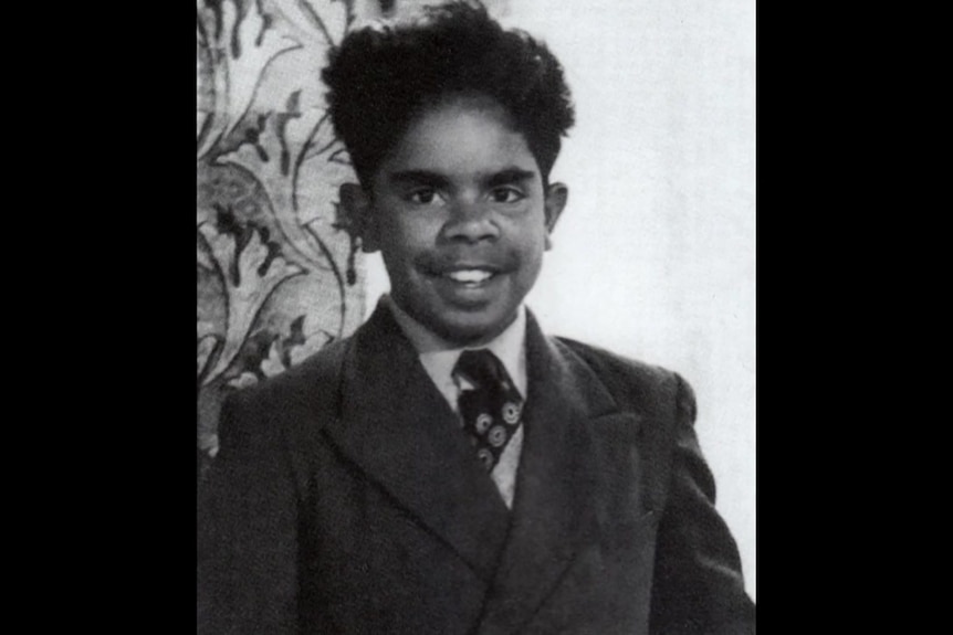 A black-and-white photograph of a smiling Uncle Jack Charles as a boy, dressed in a school uniform.