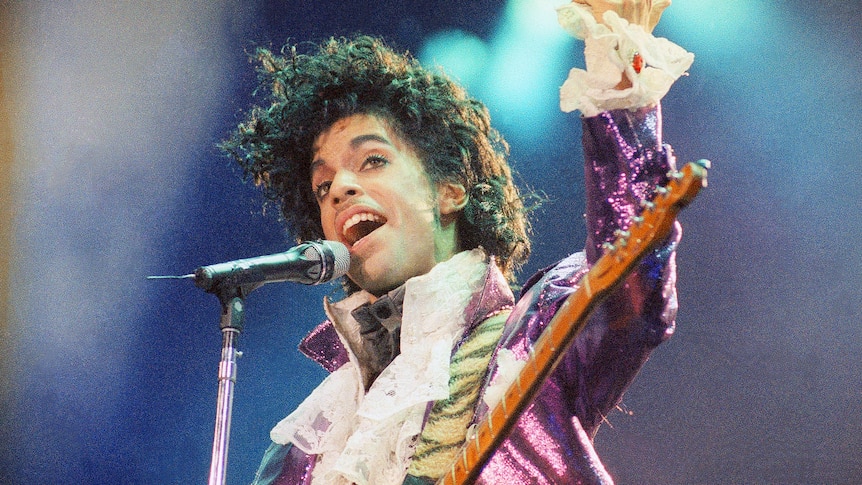 Prince peforms with a guitar wearing a puffy white shirt.