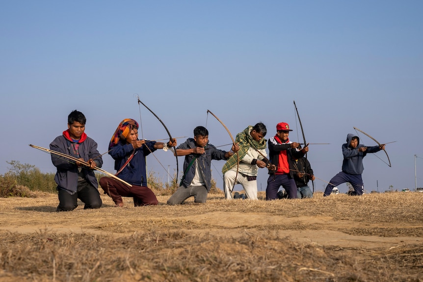 Seven men practice archery overlooking Laitlum Canyon in India