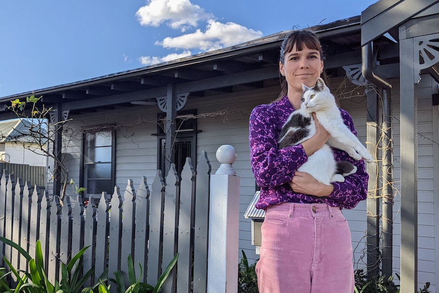 A photo of Lashea Anderson holding a cat, standing in front of a house. 
