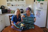 Two women sit in a kitchen holding up Twiddle Muffs