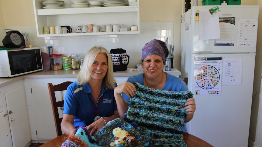 Two women sit in a kitchen holding up Twiddle Muffs