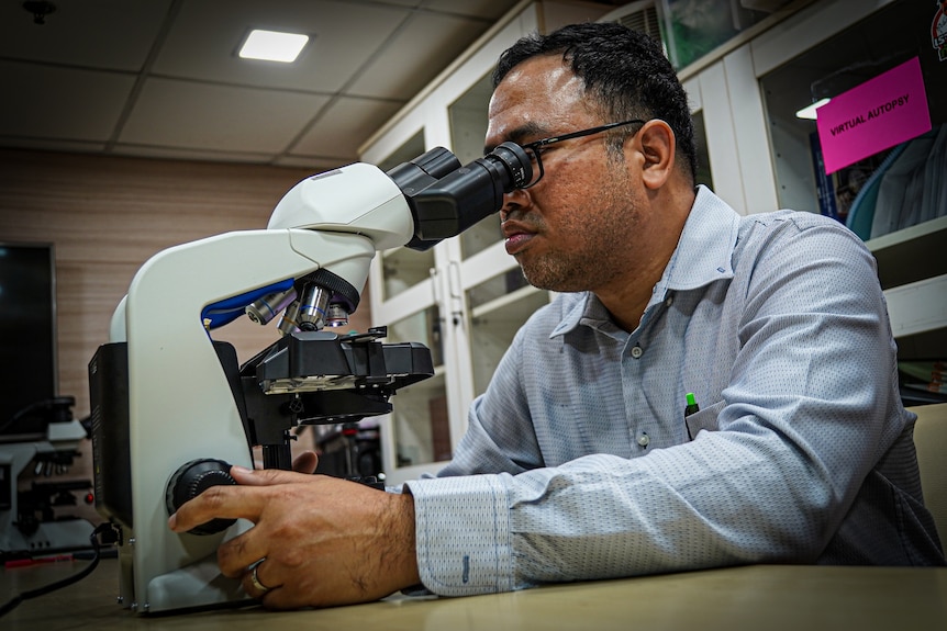A man wearing a collared shirt looks into a microscope in a lab