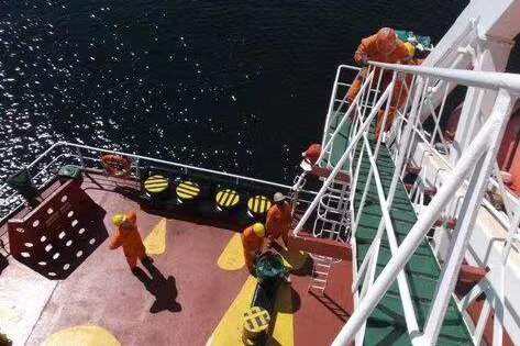 From a high vantage point atop a ladder, you look down at seafarers in orange boiler suits on a red ship's deck.