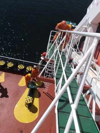 From a high vantage point atop a ladder, you look down at seafarers in orange boiler suits on a red ship's deck.