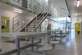 The inside of a building with dining tables, heavy cell doors and metal stairs
