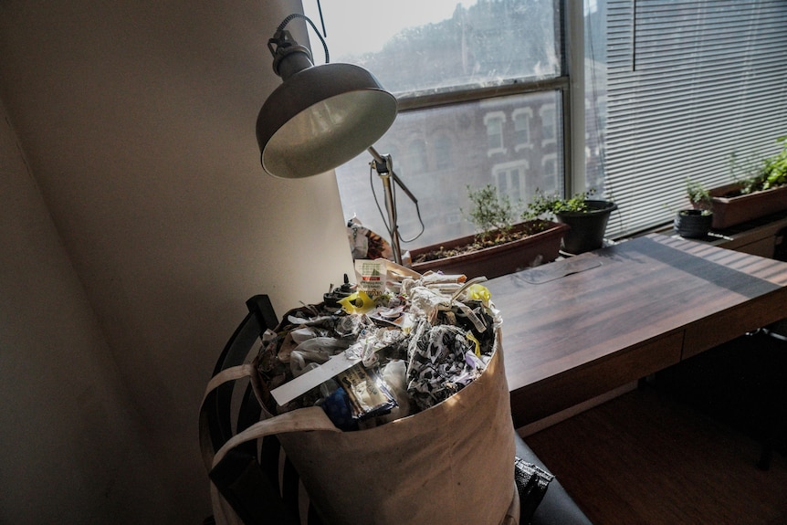 a bag of garbage sits on a chair near a window in Josh Spodek's apartment