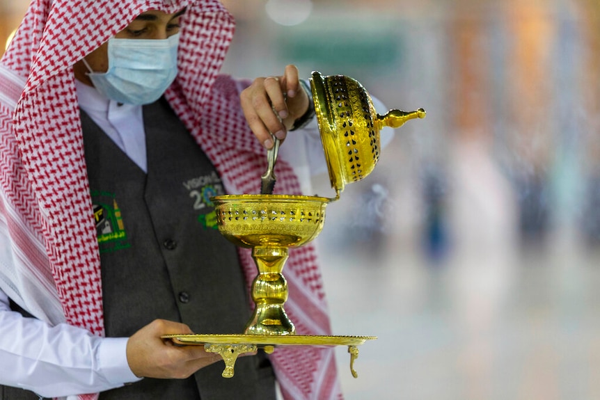 A man wearing a face mask  burns incense as the area around the Kaaba, the square structure in the Great Mosque, is prepared.