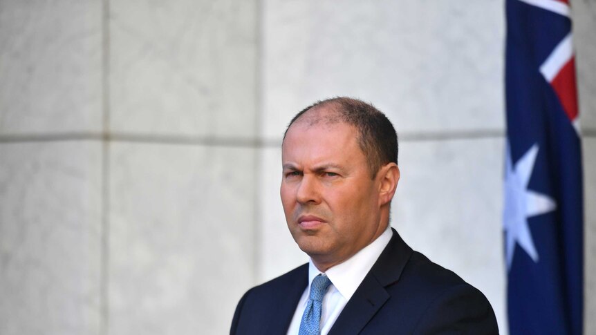 Josh Frydenberg stands in front of an Australian flag in a marble courtyard
