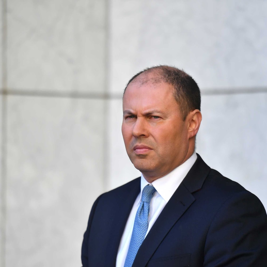 Josh Frydenberg stands in front of an Australian flag in a marble courtyard