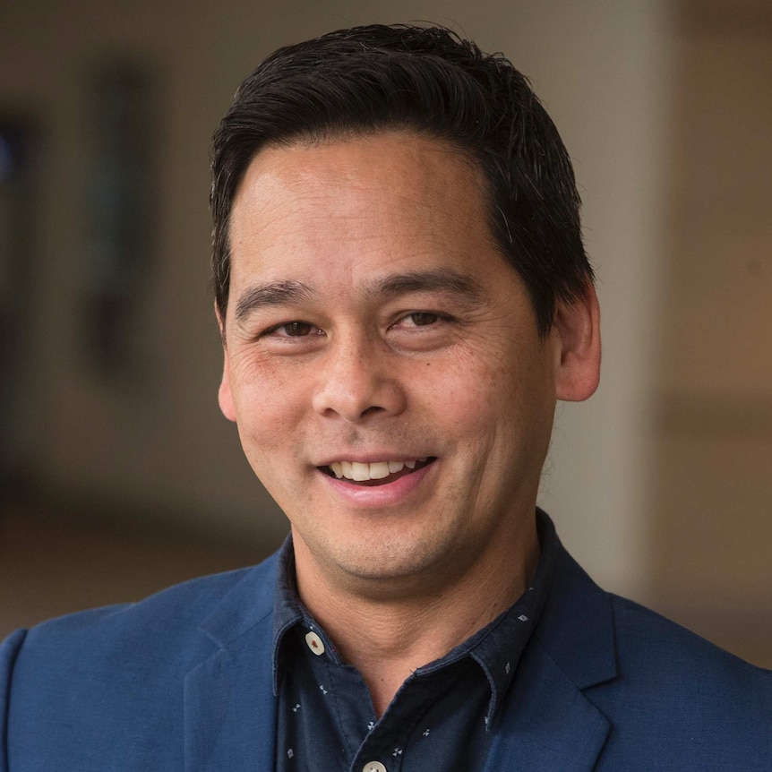 Man wearing blue blazer and collared shirt smiles at camera