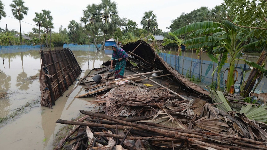 A woman gathers her belongings from a destroyed house surrounded by flood water.