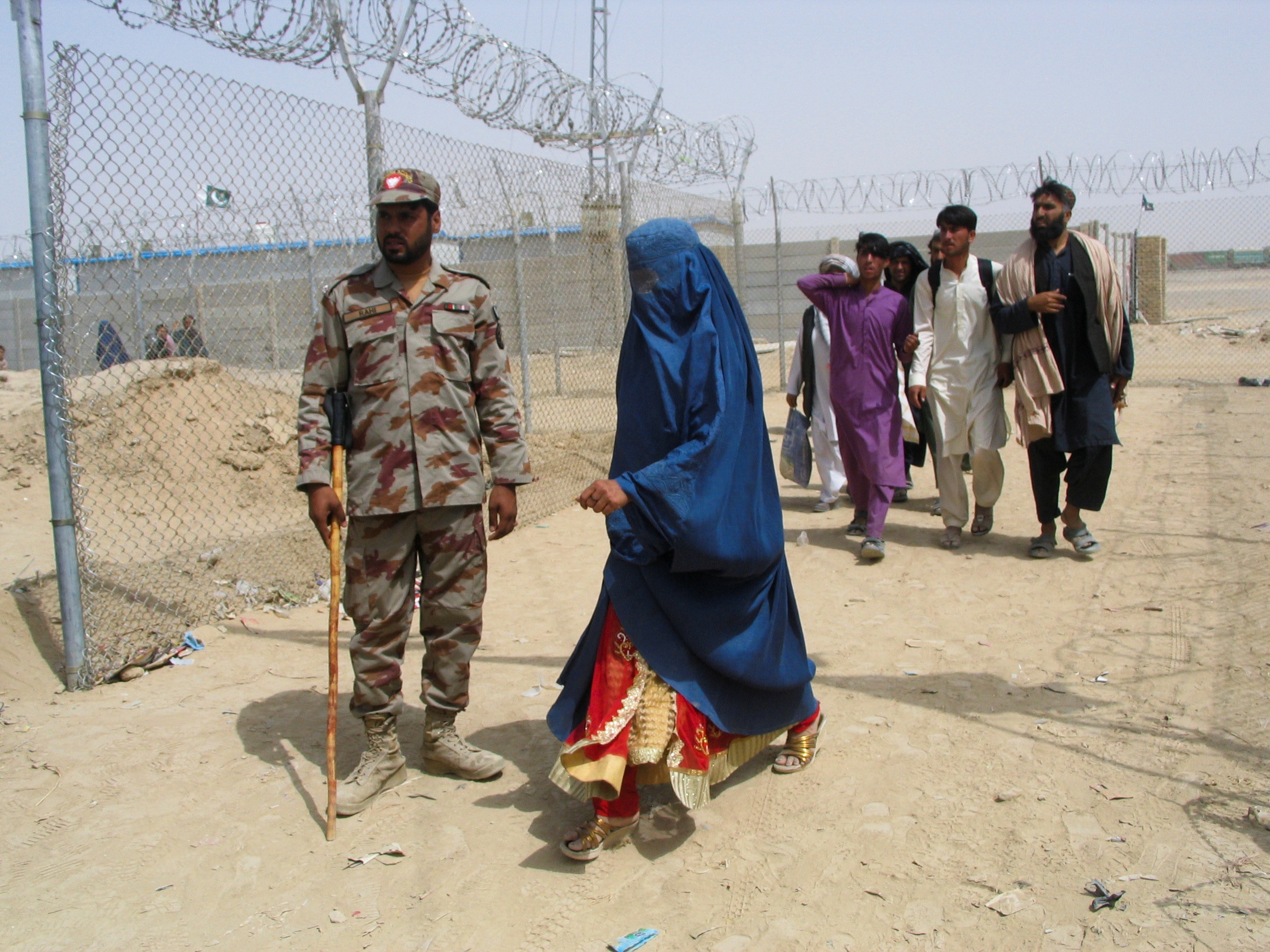 An Afghan woman in a burqa walks past a Pakistani paramilitary soldier along with others at the border checkpoint