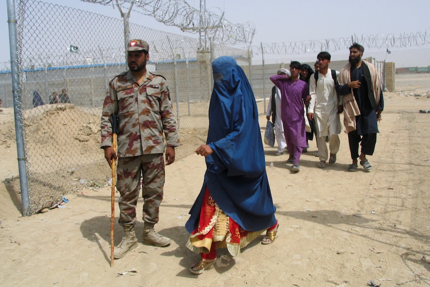 一名身穿罩袍的阿富汗妇女与其他人在边境检查站从一名巴基斯坦准军事士兵身边走过。